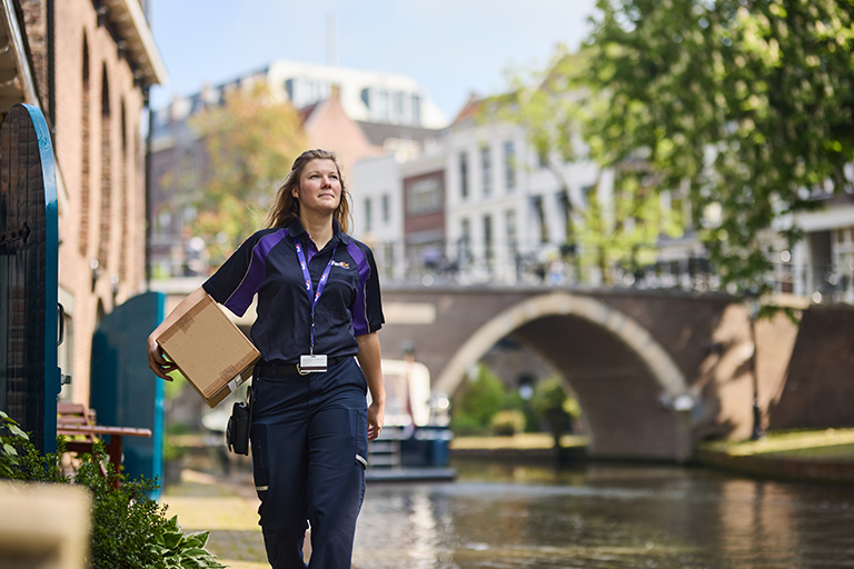 Blonde female FedEx courier carries parcel through sunny town square