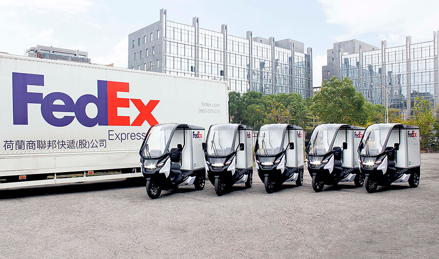 The FedEx commercial electric tricycles in front of a FedEx vehicle