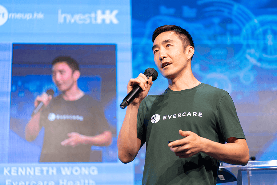 Chinese male in green ‘Evercare’ branded t-shirts on stage with microphone