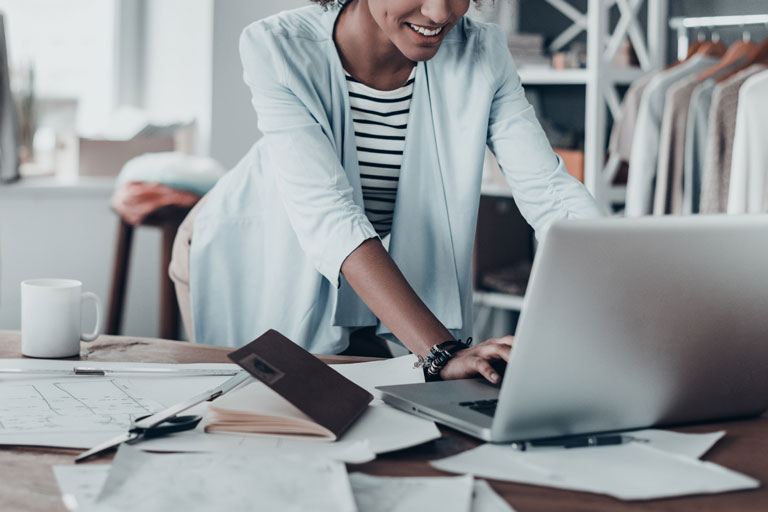 Female professional in light blue blazer leans over laptop