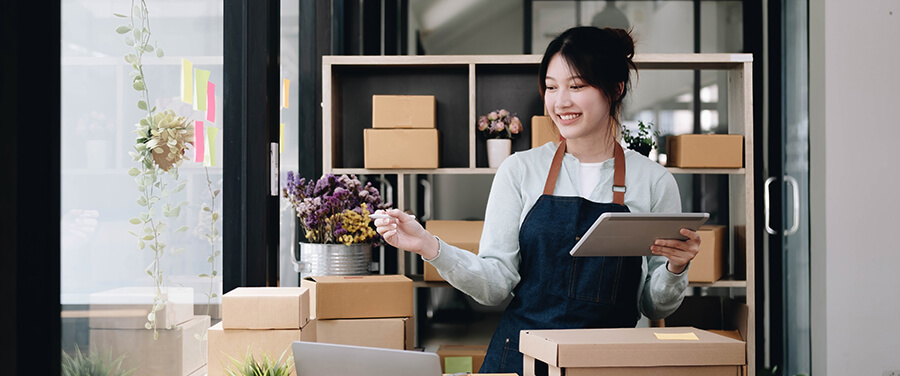 Female business owner in utility apron with mobile tablet and boxes