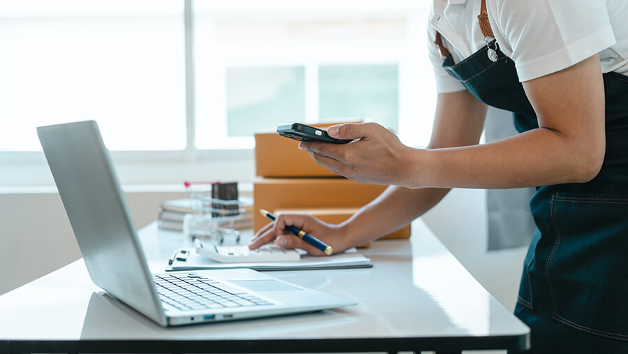 Business owner making calculations with mobile phone, laptop and pen