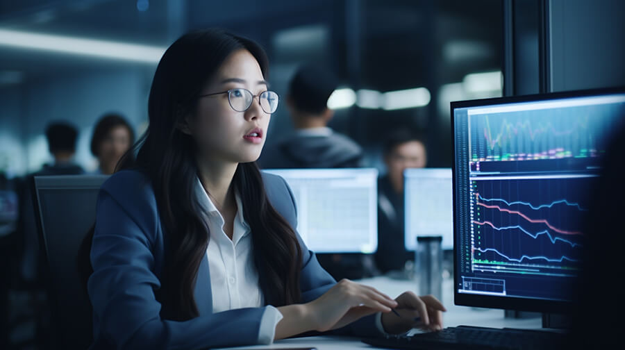 Asian female office worker wearing glasses looking at on-screen data chart