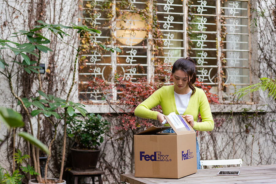 Asian female opening FedEx box in outdoor walled courtyard