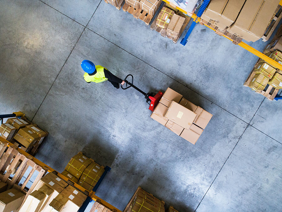 Warehouse worker in high-vis vest dragging pallet with boxes on
