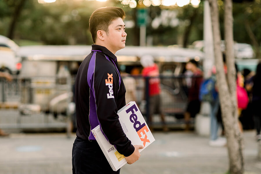Young Asian male FedEx courier staring into distance holding FedEx packet
