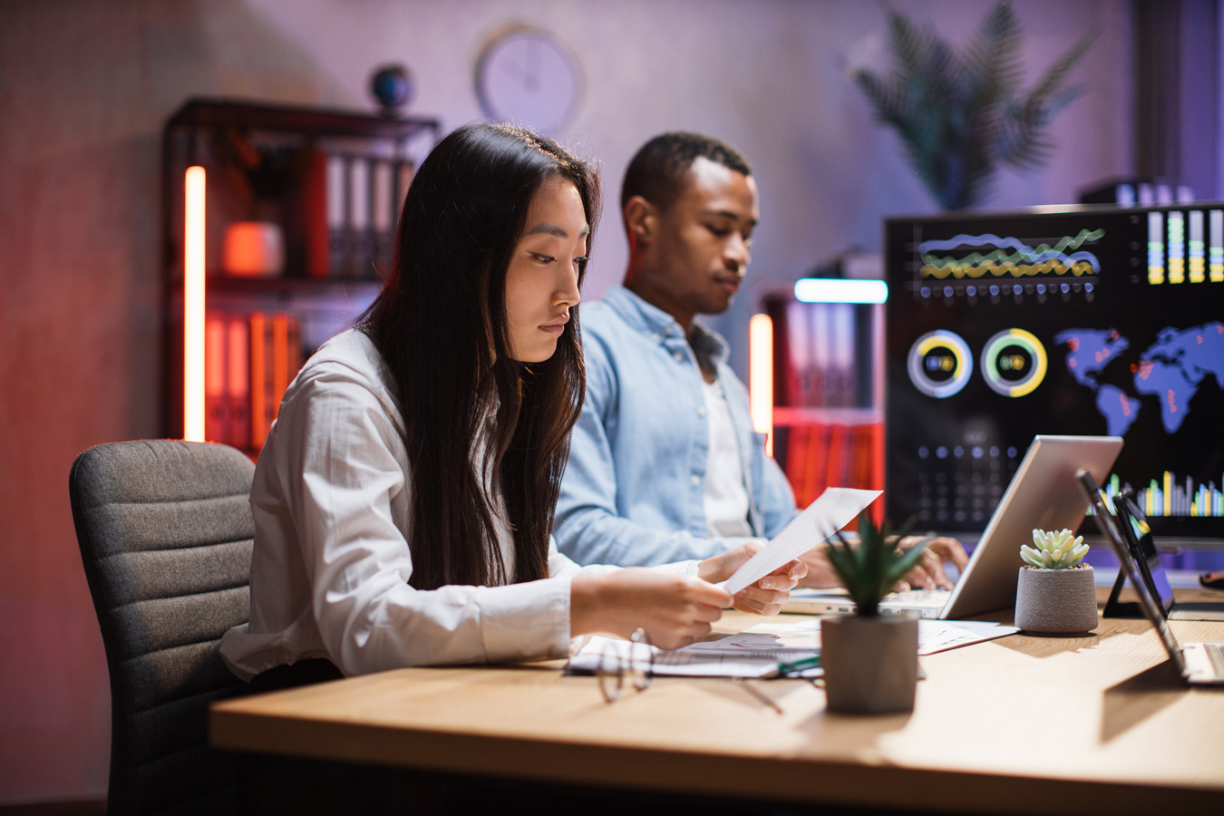 Asian female and Black male share office desk studying screens