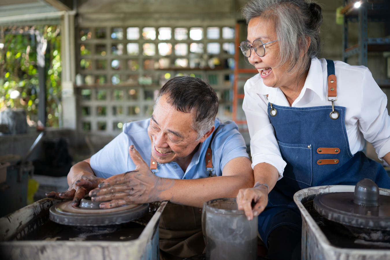 Elderly Asian male and female in aprons at pottery wheel