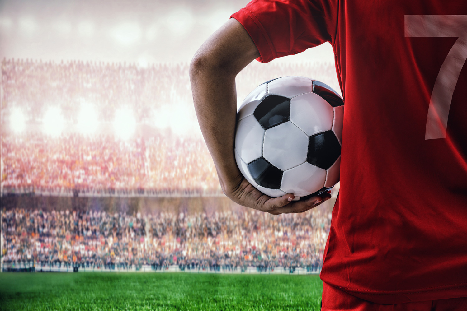 Footballer wearing red shirt with number 7 holds ball in crowded stadium