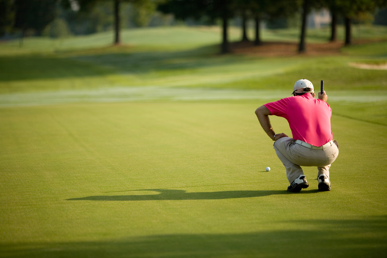 Male golfer bends down to check position of golf ball