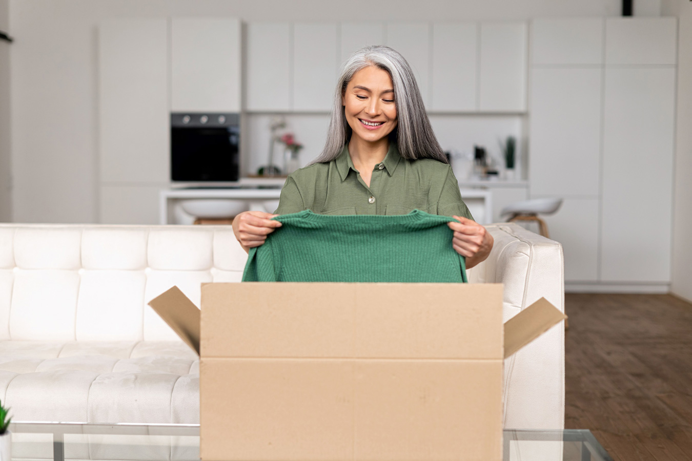Woman with long grey hair unpacks jumper from cardboard box