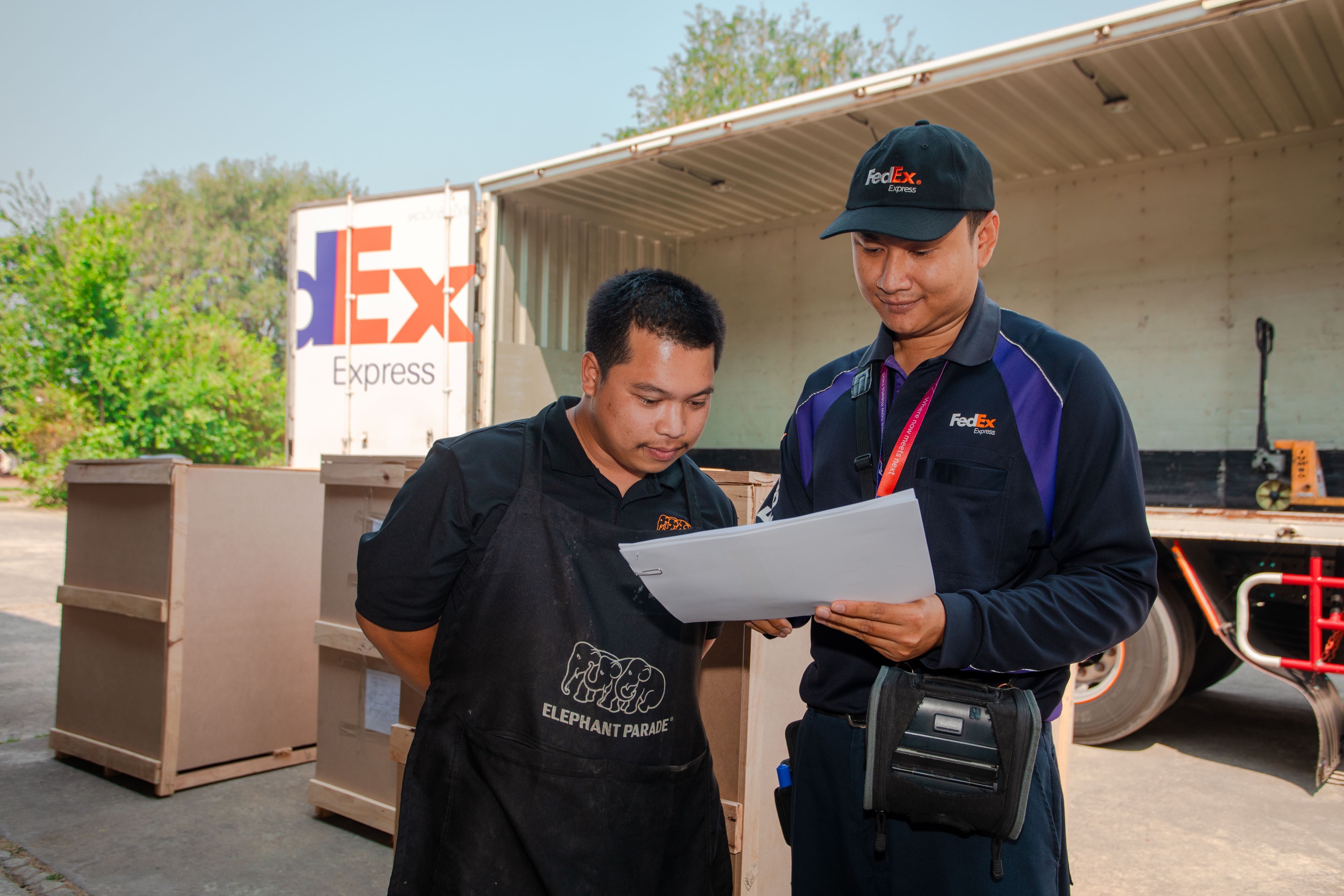 A FedEx courier and a man from Elephant Parade looking at a document in front of a FedEx delivery truck