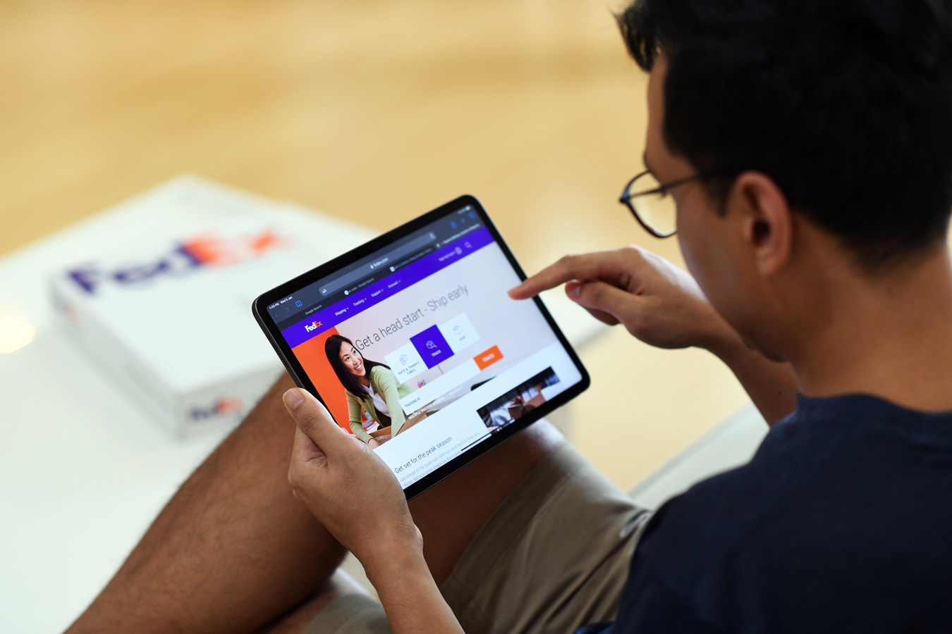 Asian male wearing glasses browses FedEx website on mobile tablet