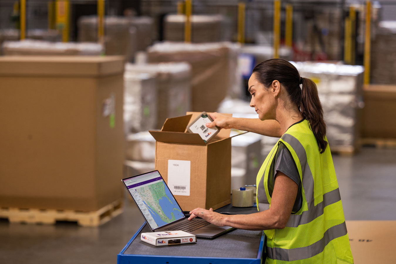 European female wearing high-vis vest scans items for FedEx boxes