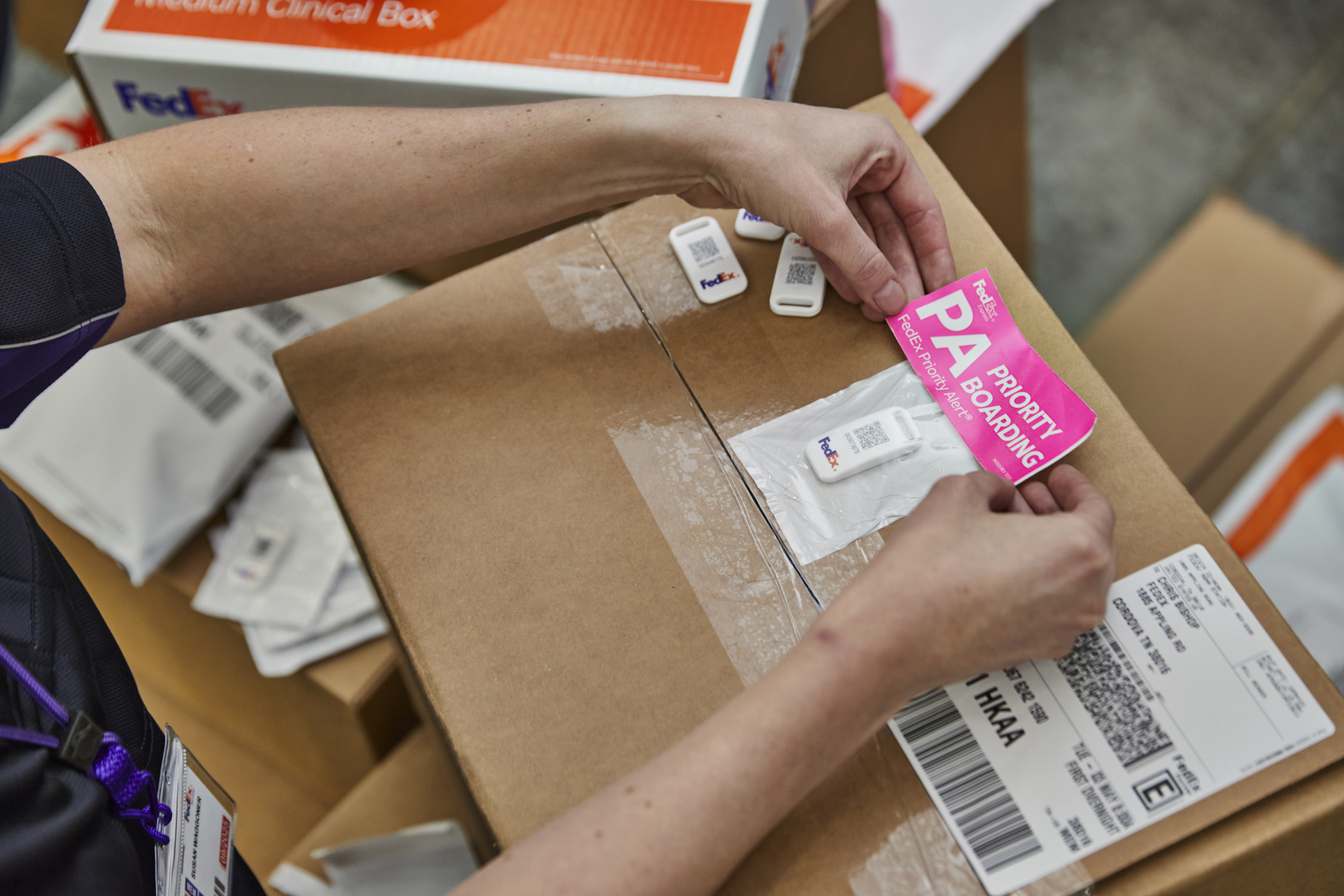 Pink ‘Priority Boarding’ sticker being applied to FedEx boxes with sensor tag on