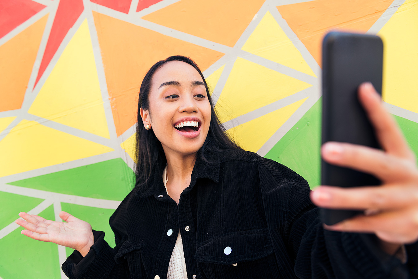 Happy Gen Z female laughing on video call next to multicolored wall