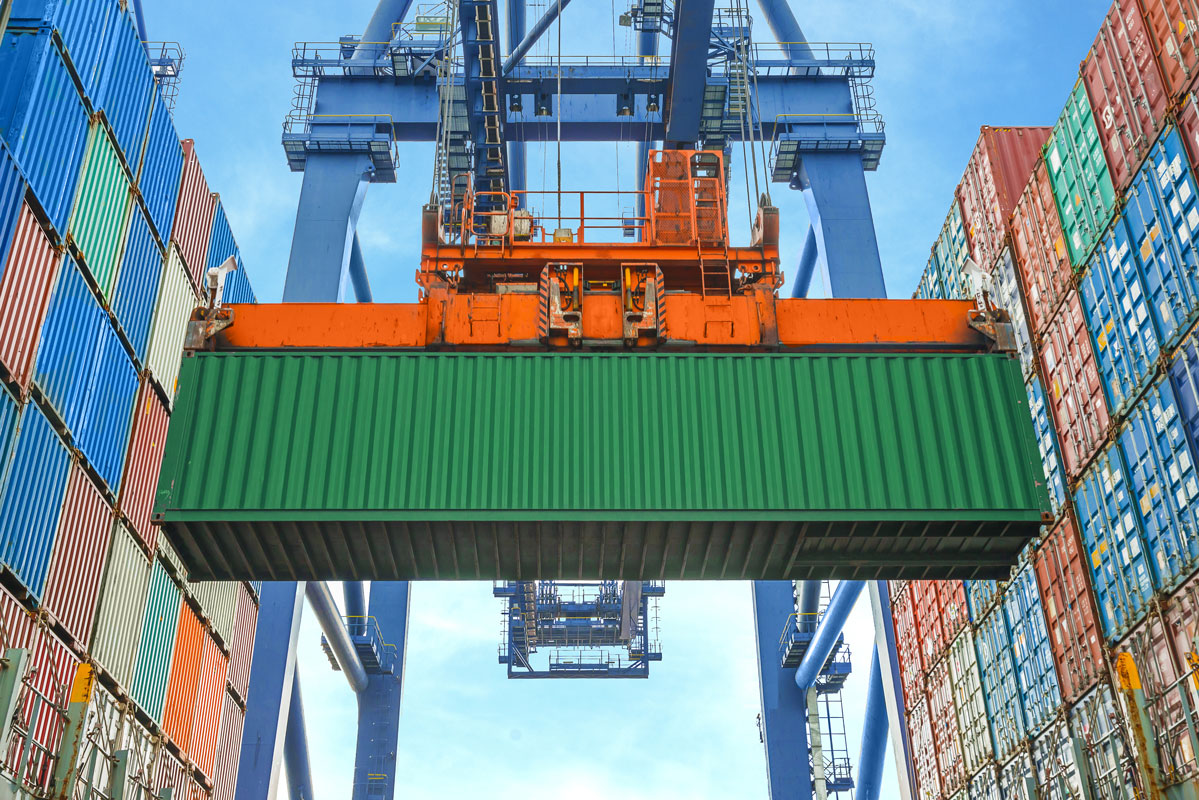 Orange shipping container lifted into air at container warehouse