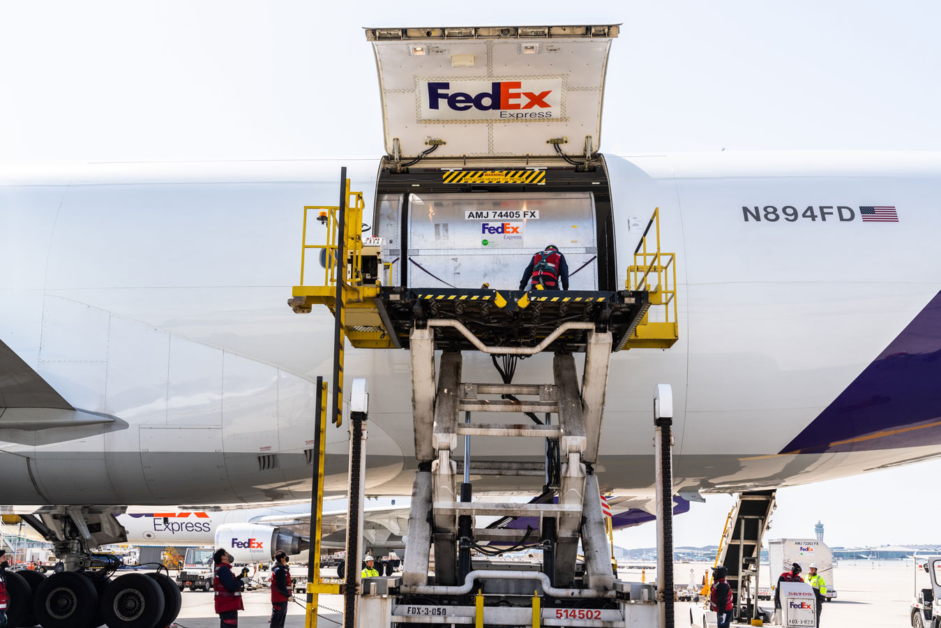 Team of workers using hydraulic ramp to load cargo into FedEx plane