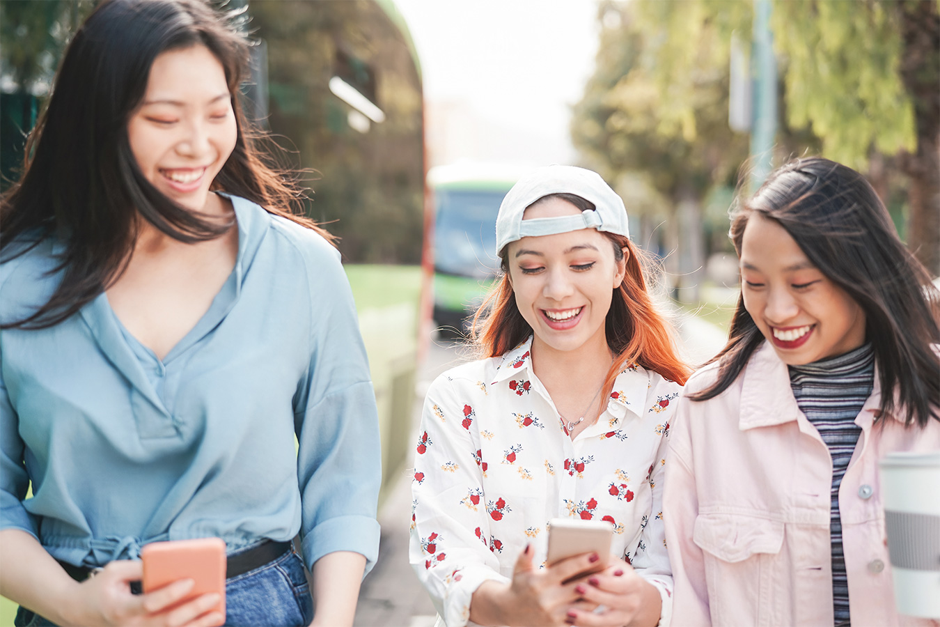 Three Gen Z Asian female friends laughing with mobile phones