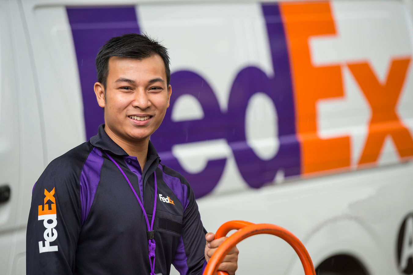 A smiling FedEx employee stands before a delivery van.