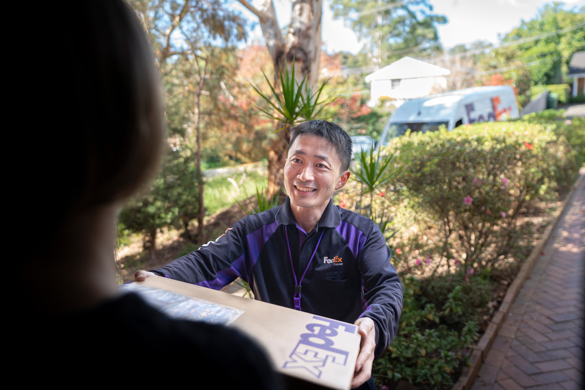 Male Asian FedEx courier hands over parcel on suburban street