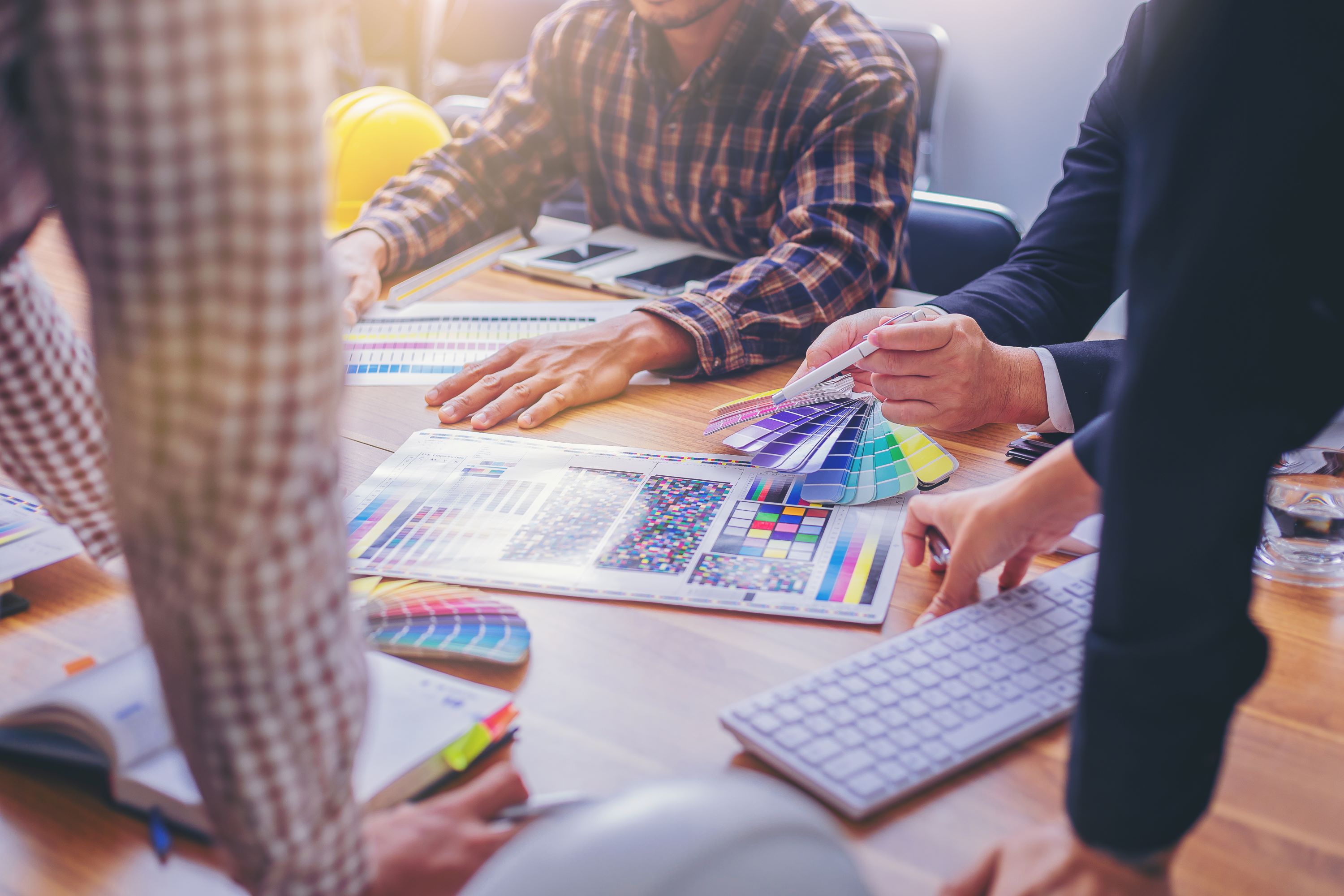 Group of professionals collaborate at shared desk, comparing color charts