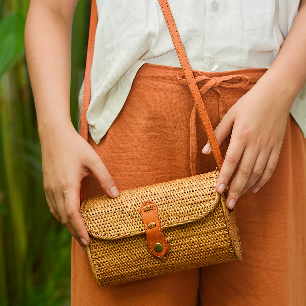 Woman in orange trousers shows off cross-body wicker handbag